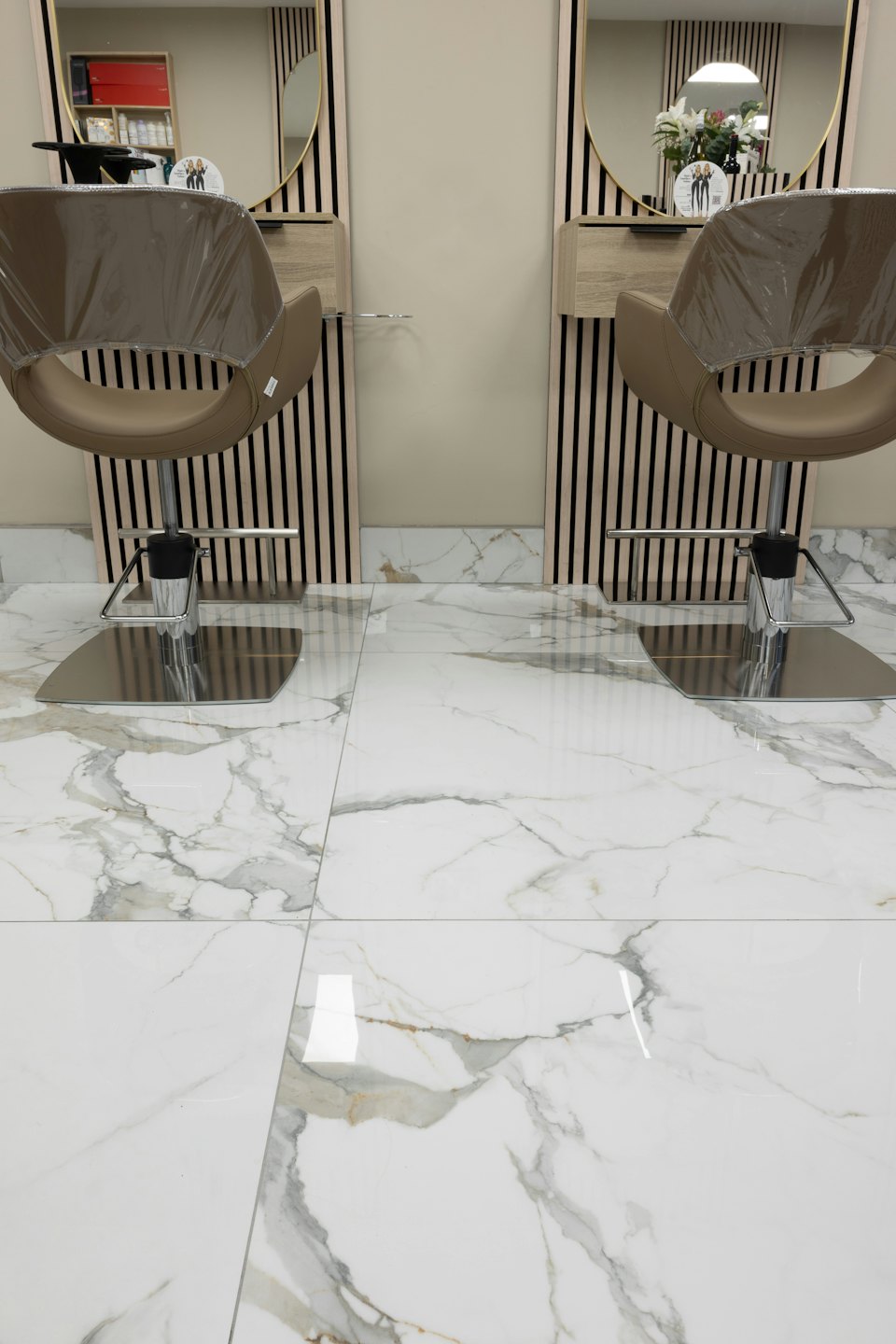 Two modern hair salon chairs with gold-framed mirrors.