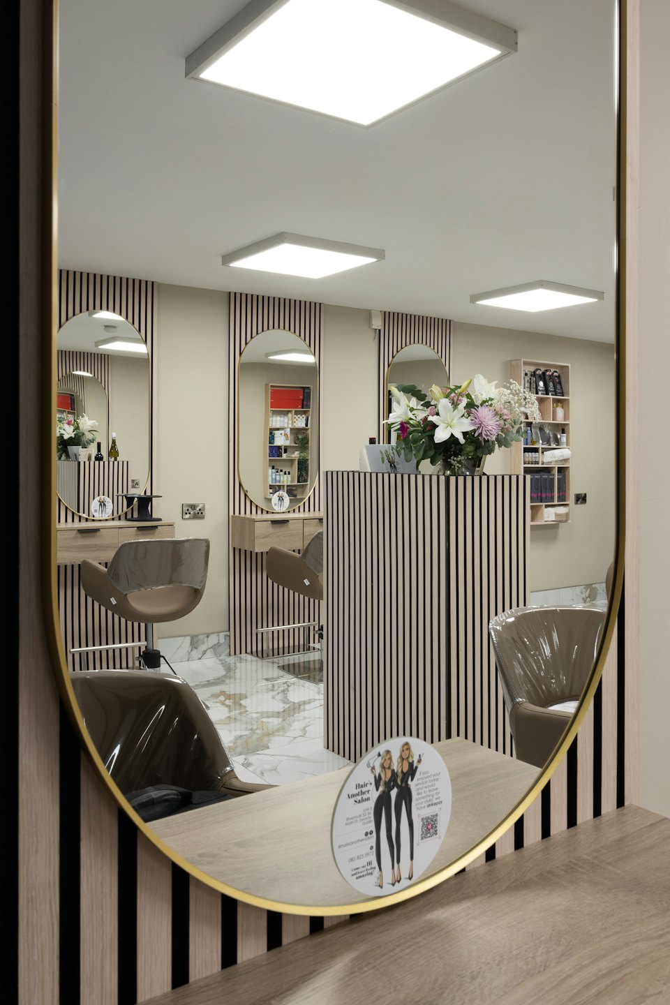 Modern hair salon interior reflected in a large gold-framed mirror.