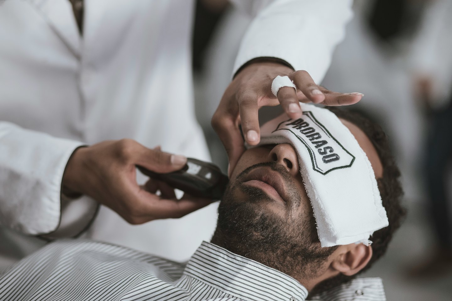 Barber trims customer's beard with electric trimmer.