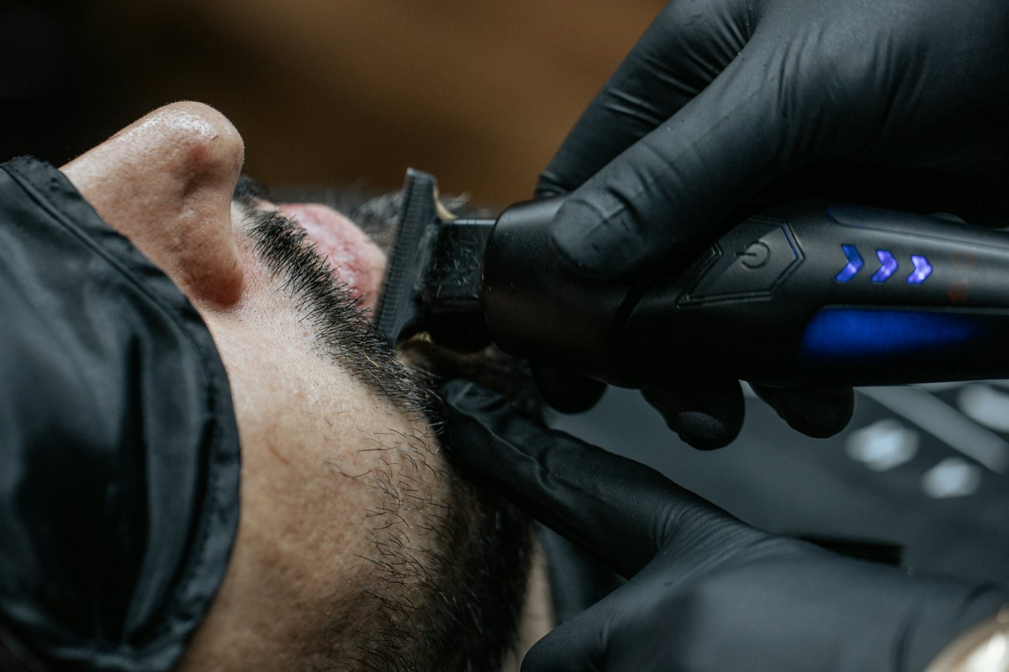 A barber uses electric clippers to trim a customer's beard.